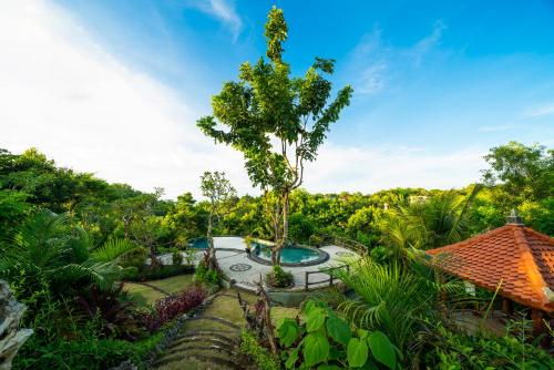 a garden with a swimming pool and a tree at Ring Sun Cottages in Uluwatu