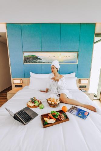 a woman laying on a bed with a plate of food and a laptop at Sala Grand Tuy Hoa Hotel in Tuy Hoa