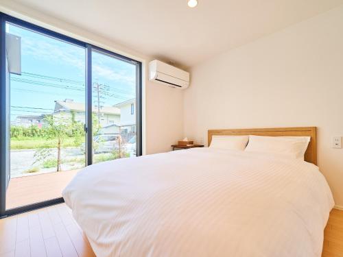 1 dormitorio con cama blanca y ventana grande en Rakuten STAY HOUSE x WILL STYLE Miyazaki Aoshima 101 en Miyazaki