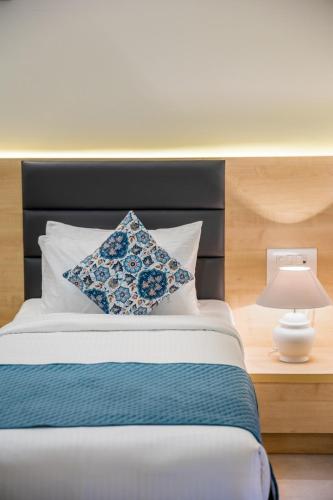a bed with a blue and white pillow and a lamp at Iris Suites in Bengaluru