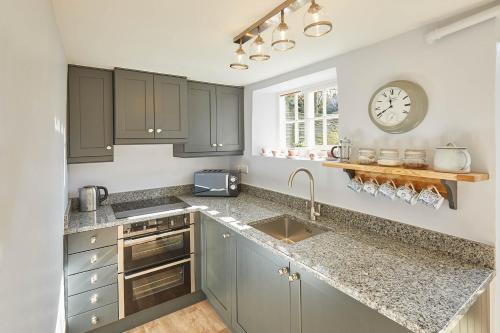 a kitchen with gray cabinets and a clock on the wall at Host & Stay - Holmlea Cottage in Lockton
