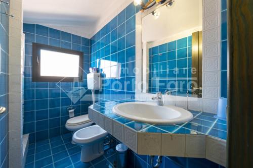 a blue tiled bathroom with a sink and two toilets at 18 BAIA FARO - Grazioso bilocale mansardato a Baia del Faro in Palau