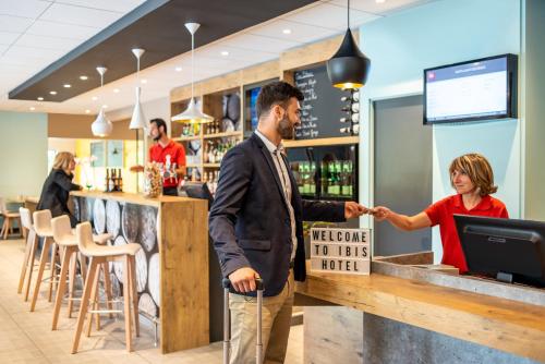 a man and a woman standing at a bar at ibis Nuits Saint Georges in Nuits-Saint-Georges
