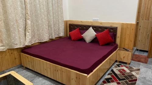 a wooden bed with red and white pillows on it at Tulip Flowing River View Hotel. in Shamshi