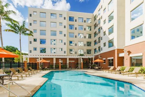 a pool with chairs and umbrellas in front of a hotel at Hyatt House Fort Lauderdale Airport/Cruise Port in Dania Beach