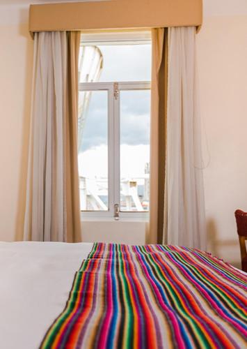 a bed with a colorful blanket in front of a window at Hotel de Turistas Huancayo - Hotel Asociado Casa Andina in Huancayo
