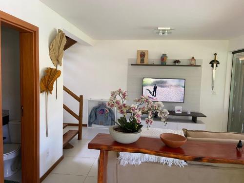 a living room with a tv and a table with flowers at CASA PRAIA DO FORTE in Mata de Sao Joao