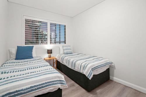 two beds in a room with a window at Cosy Beachside Unit, Short Stroll to the Beach in Terrigal