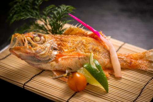 a piece of fish on a bamboo plate with a cherry tomato at Kawaguchiya Kinosaki Riverside Hotel in Toyooka