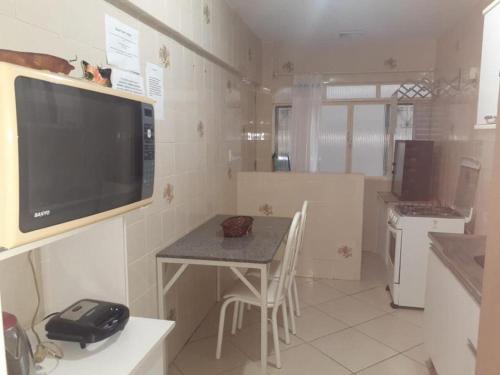 a kitchen with a table and a television on the wall at Ape agradável a 50 m das piscinas de Piratuba in Piratuba