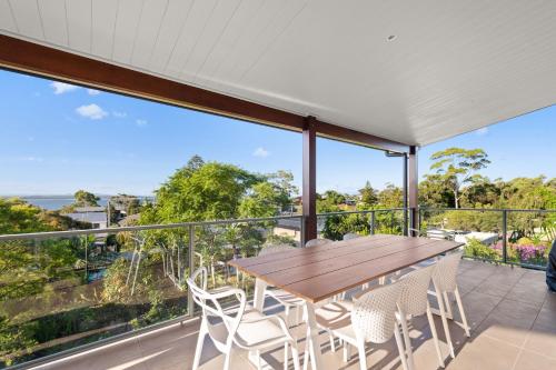 a balcony with a wooden table and white chairs at Wahgunyah Road 52 in Nelson Bay