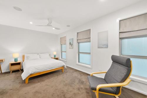 a white bedroom with a bed and a chair at Wahgunyah Road 52 in Nelson Bay