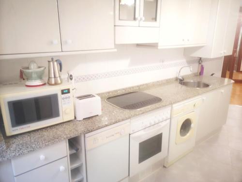 cocina blanca con microondas y fregadero en Apartamento CONFORT BEACH, 300 mtr playa, en Gijón
