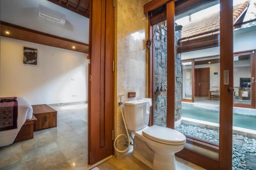 a bathroom with a toilet and a swimming pool at Gigimas Private Villa in Ubud