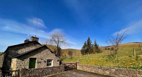 an old stone house in a field with a fence at Cross Haw Cottage in Sedbergh
