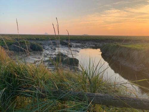 a river in the middle of a field at sunset at Gîtes grands groupes - Château des Forges Gouville in Gouville-sur-Mer