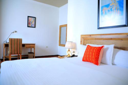 a white bed with a red pillow and a desk at Victoria Hotel Apartment in Addis Ababa