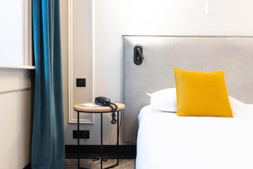 a bed with a yellow pillow and a phone on a table at Best Western Urban Hotel in Lille