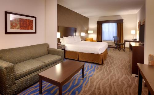 Holiday Inn Express & Suites Overland Park, an IHG Hotel في أوفرلاند بارك: غرفه فندقيه بسرير واريكه وطاولة