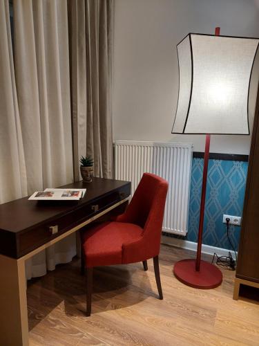 a desk with a red chair and a lamp at Somerset City Centre Atyrau in Atyraū