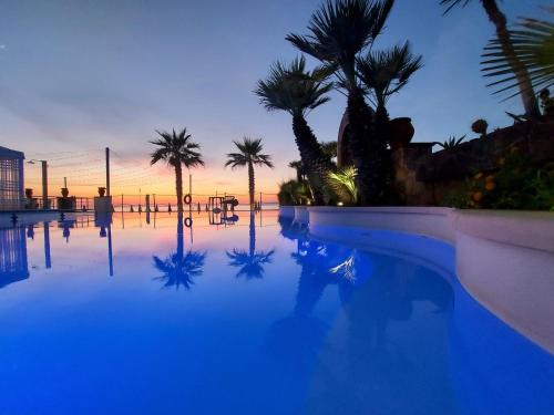a swimming pool with palm trees and a sunset at Hotel Il Gabbiano Beach in Terme Vigliatore
