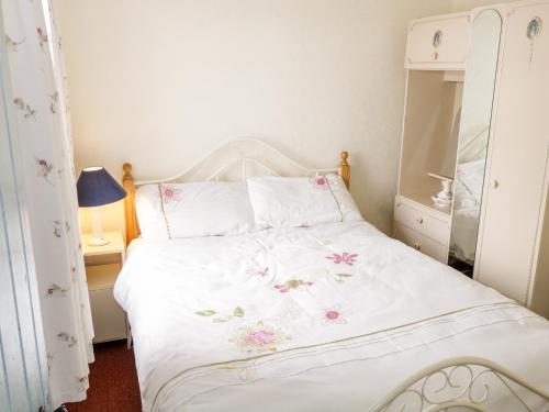a bedroom with a white bed with pink flowers on it at The Cottage in Carrowsallagh Bridge