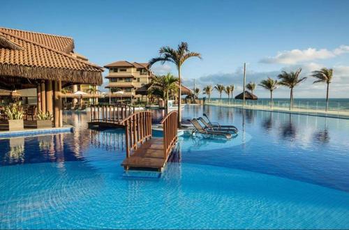 a resort swimming pool with chairs and palm trees at Manhattan Beach Riviera in Aquiraz