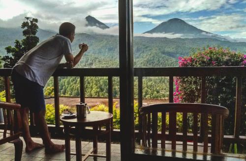 a man standing on a balcony looking out at a mountain at Made Oka Homestay and Warung in Munduk