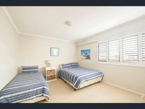 two beds in a bedroom with white walls and windows at Beachside 4 in Tuncurry