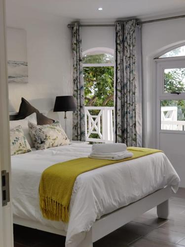 a white bed with a yellow blanket and two windows at 44 Montego Bay Caribbean Estates in Port Edward