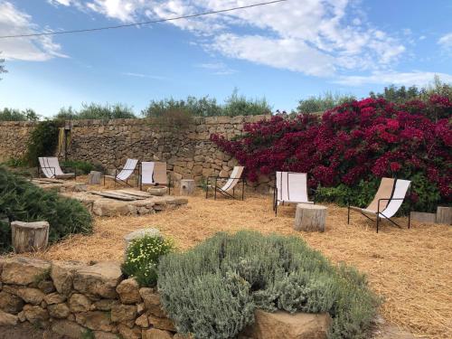 a group of chairs sitting in a yard next to a stone wall at Casette Marianeddi -Agriturismo Marianeddi in Noto