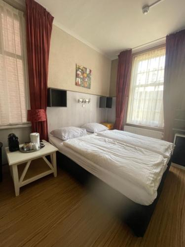 a bedroom with a bed and a table and windows at Pension de Zeeschelp in Domburg