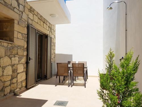 a patio with a table and chairs and a stone wall at New Villa Kalimera, view to Falasarna beach in Plátanos