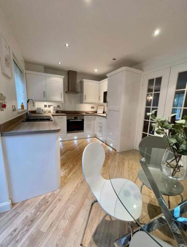 una cocina con armarios blancos y una mesa y sillas de cristal. en Modern + Secluded 3 bed, 10 mins into city centre en Spixworth