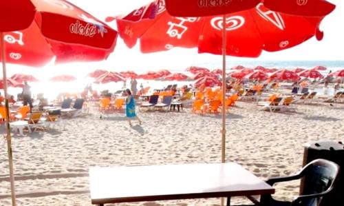 a sandy beach with red umbrellas and chairs and tables at Hotel Apartment TLV-bat yam 81 in Bat Yam