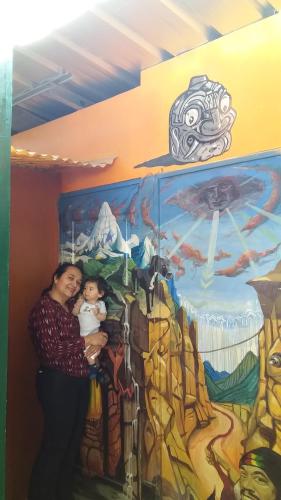 a woman holding a baby in front of a mural at Monkeywasi Climbing Hostel in Huaraz