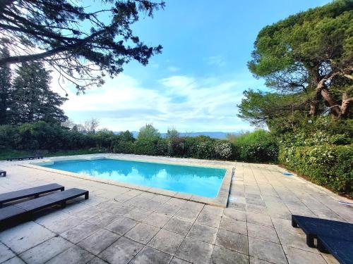 a swimming pool on a patio with benches and trees at Mazet du Château Joyeux de Violet in Pépieux