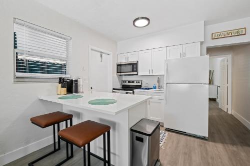 a white kitchen with a refrigerator and two bar stools at Comfy BNB w/ King Bed + Work/Travel + Beach 8 Min in Hallandale Beach