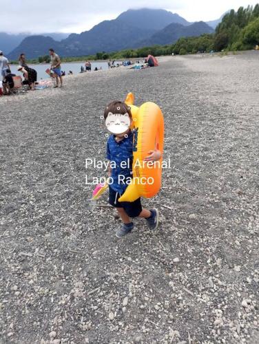 a child standing on a beach with an orange life vest at Casa de campo Llifén Futrono Lago Ranco in Ranco