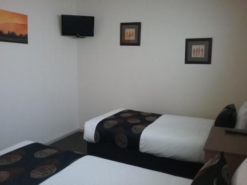 a room with two beds and a tv on the wall at Werribee Park Motor Inn in Werribee