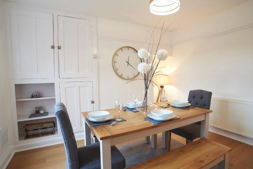 a dining room table with chairs and a clock on the wall at Doctors lane Stylish 3 Bedroom Family House with Parking in Melton Mowbray