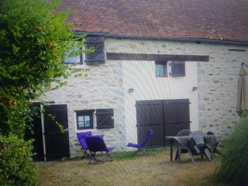 un grupo de sillas púrpuras y una mesa frente a un edificio en La croix des Landes gîte ou chambre d'hôte avec piscine à Chouvigny, en Chouvigny