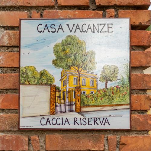 a sign on a brick wall with a yellow house at LA CONCHIGLIA località Caccia e Riserva in Santa Marinella