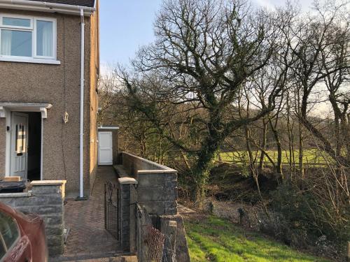 a house with a tree next to a driveway at 3br-Sleeps6-Garden-Mountain &near 4 Falls Walks on in Pont-Nedd-Fechan