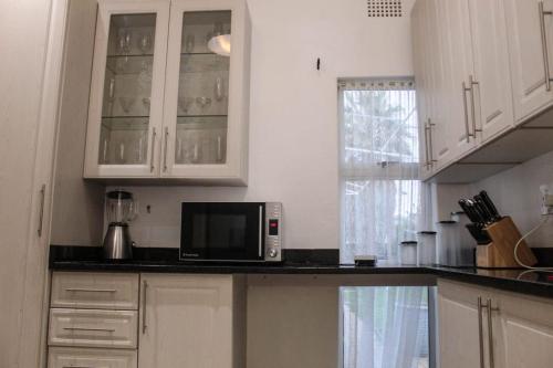 a kitchen with white cabinets and a microwave on a counter at Semeni Asante Guesthouse in Johannesburg