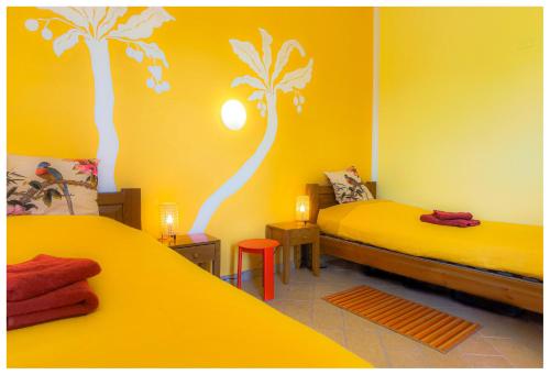 two beds in a room with yellow walls and palm trees at Hostel Vela Vega in Butera