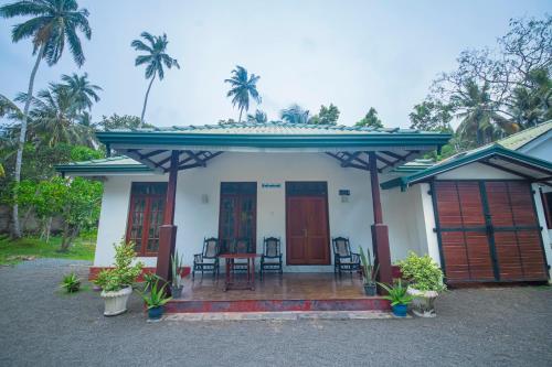 uma casa branca com um alpendre com cadeiras e palmeiras em The Esence of Sri Lanka em Ahungalla