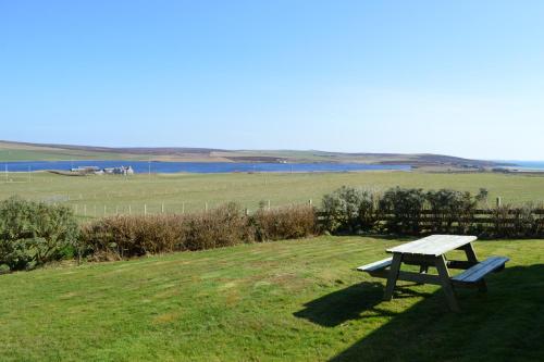 a picnic table in a field with a view of the water at Bachylis Self Catering in Kirkwall