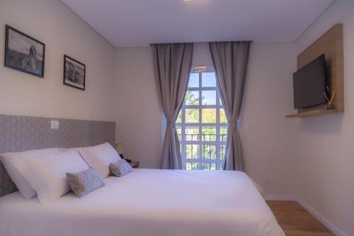 a bedroom with a white bed and a window at Village de Charme - 2km do Capivari in Campos do Jordão