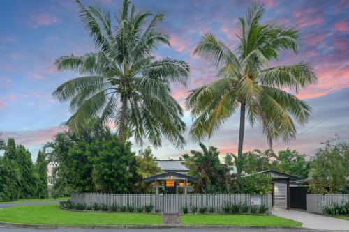 deux palmiers devant une maison avec une clôture dans l'établissement Sweet Creek Cottage, Palm Cove, 200m to Beach, Heated Pool, Pets, à Palm Cove